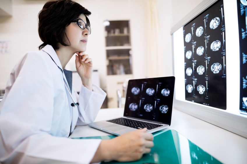 Doctor reviews scans on a lightboard and laptop.