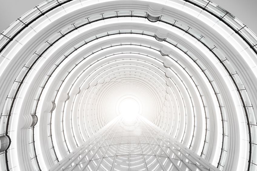 An interior view of a long, cylindrical building with a series of structural supports, creating a repetitive pattern along its length, with a bright light at the far end