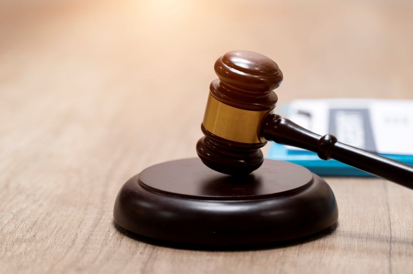 A close-up of a wooden gavel on a sound block, with blurred documents in the background