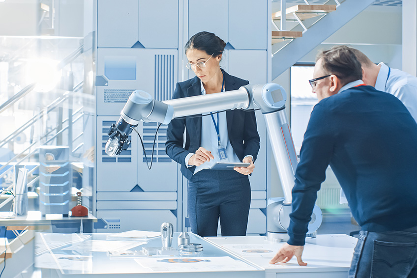 Three business people working alongside a robotic arm