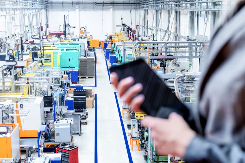 Image of a businesswoman holding a tablet in a large manufacturing space