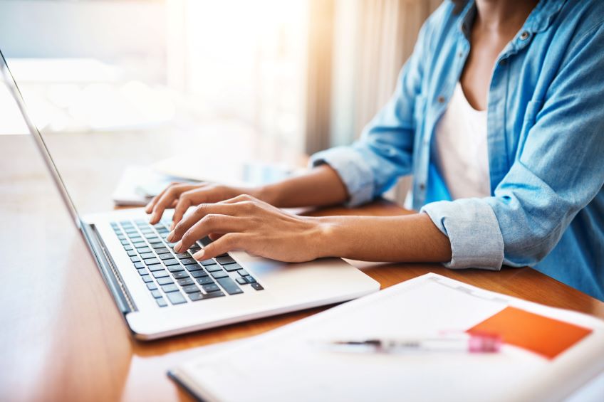 Woman sitting at a table with a laptop and pen and paper.