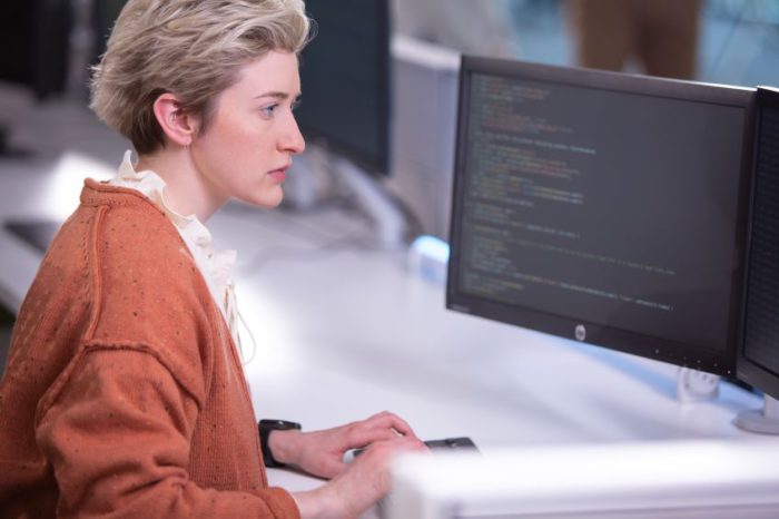 Woman sitting at a desk, looking at code.