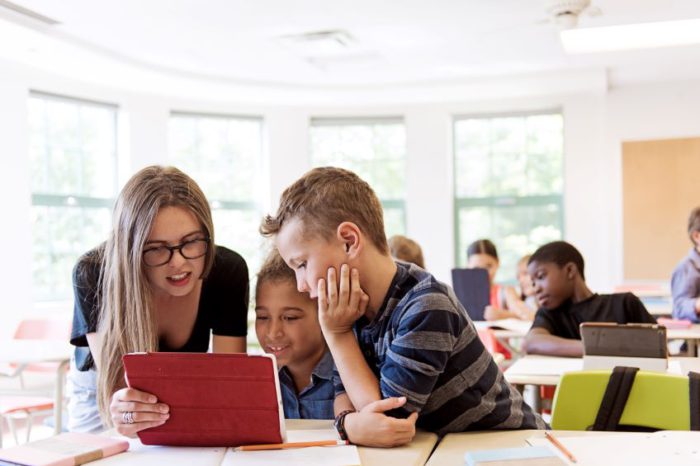 Image of three students in a classroom looking at a tablet together.