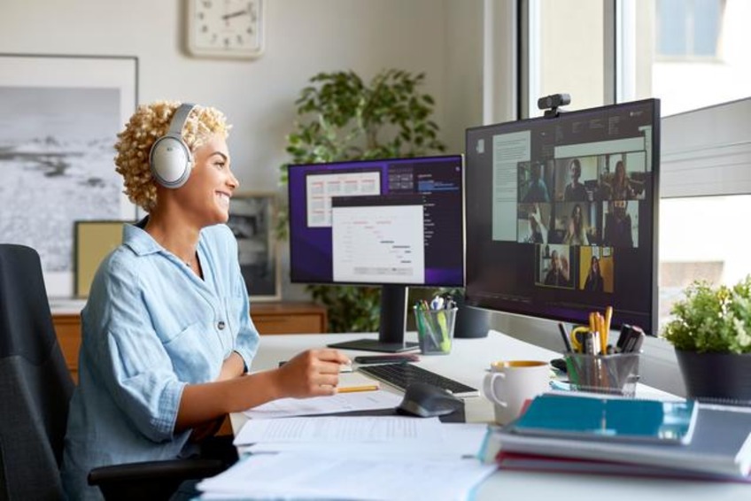 Cheerful businesswoman holding document during video conference with colleagues. Smiling blond Afro female professional is working at home office. She is wearing wireless headphones.